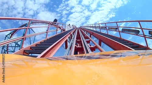 Roller coast heading up hill toward blue and cloudy sky.