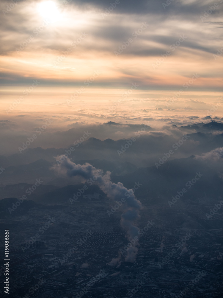 Toned image of smog over Beijing plant with a large column of toxic smoke in the background of a sunset with mountains and cumulus clouds