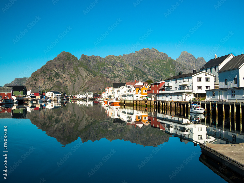 Image of Henningsvaer city sea bay with boats on a background of big mountains and clear skies