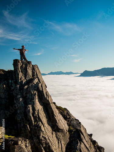 Toned image adult woman with a backpack with arms outstretched stands on the edge of a cliff and looking at the sunrise against the blue sky and thick clouds floating down © atomfotolia