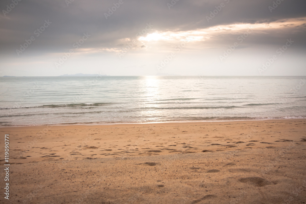 Tranquil sea at deserted sunset beach in soft tones with sunlight shining through the clouds