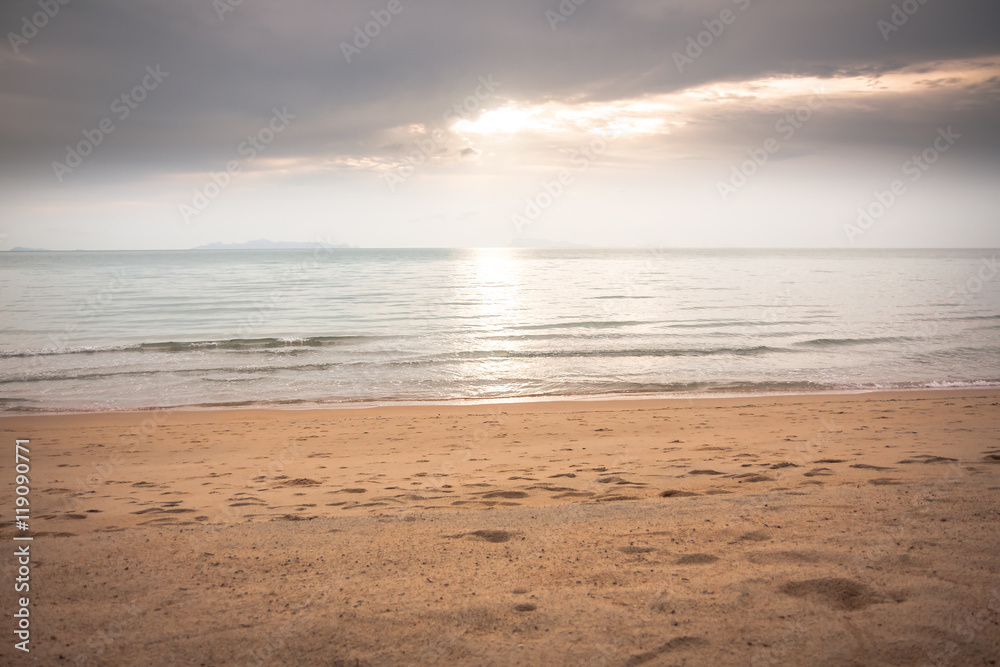 Tranquil sea at deserted sunset beach in soft tones with sunlight shining through the clouds Tranquil sea at deserted sunset beach in soft tones with sunlight shining through the clouds