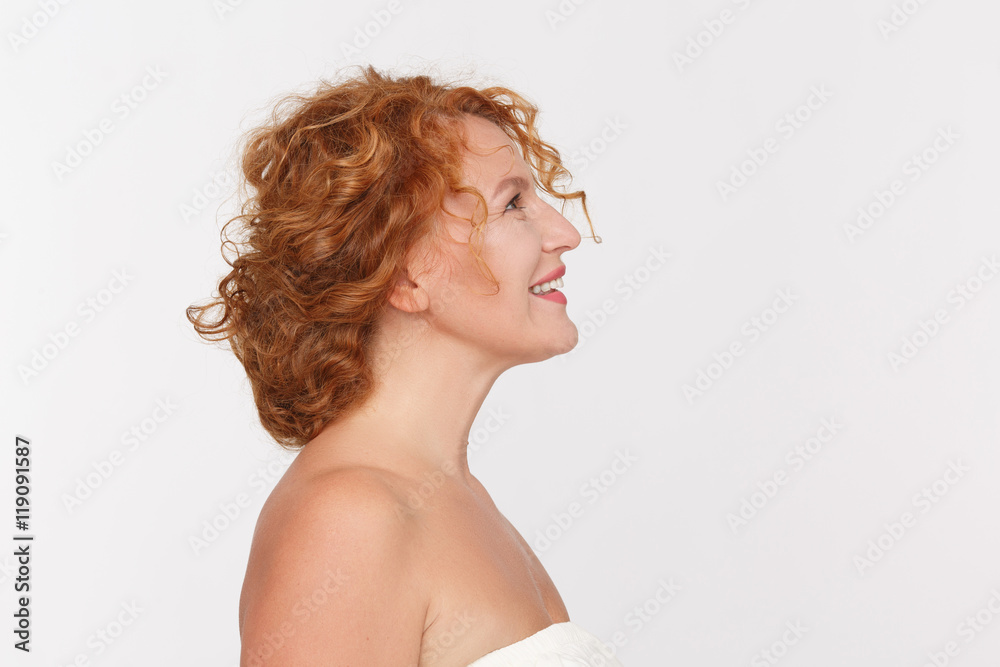 Closeup profile of happy mature woman smiling and looking upwards. Beautiful red haired lady posing isolated on white background in studio. Closeup profile of happy mature woman smiling and looking upwards. Beautiful red haired lady posing isolated on white background in studio.