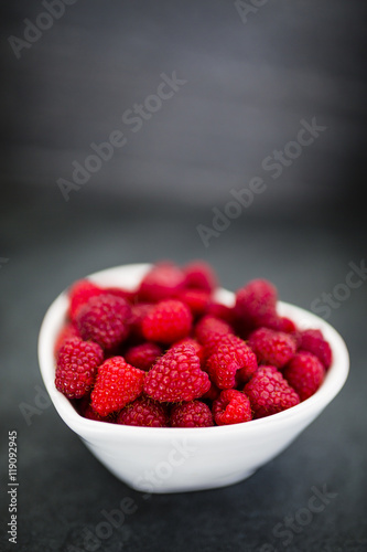 Fresh raspberries in bowl on dark background with space for text.