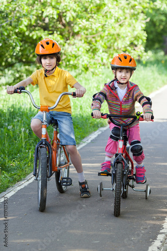 A little girl and boy in helmet riding a bicycle in park