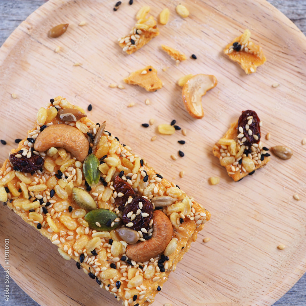 Top view of healthy crispy cereal bar or muesli bar with pumpkin seeds, sunflower seed, sesame, nuts and dried fruits with honey in a wooden plate. Top view of healthy crispy cereal bar or muesli bar with pumpkin seeds, sunflower seed, sesame, nuts and dried fruits with honey in a wooden plate.