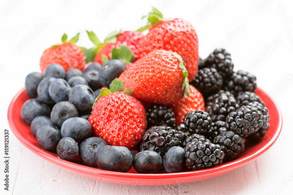 red plate full of ripe berries on white wood red plate full of ripe berries on white wood
