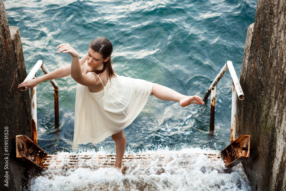 Young beautiful ballerina dancing and posing outside, sea background