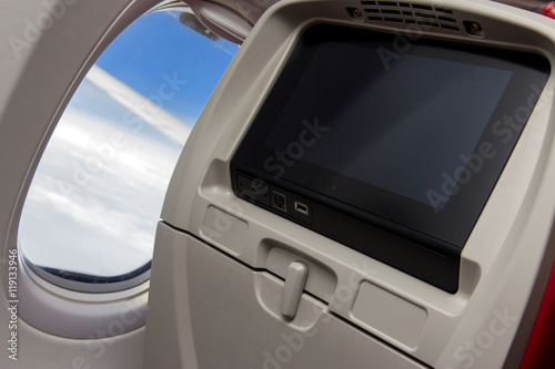 seat with a monitor beside the window of a flying airplane