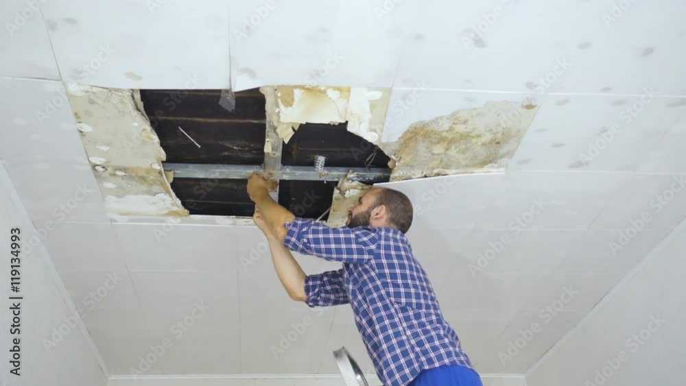 Man repairing collapsed ceiling. Ceiling panels damaged huge hole in