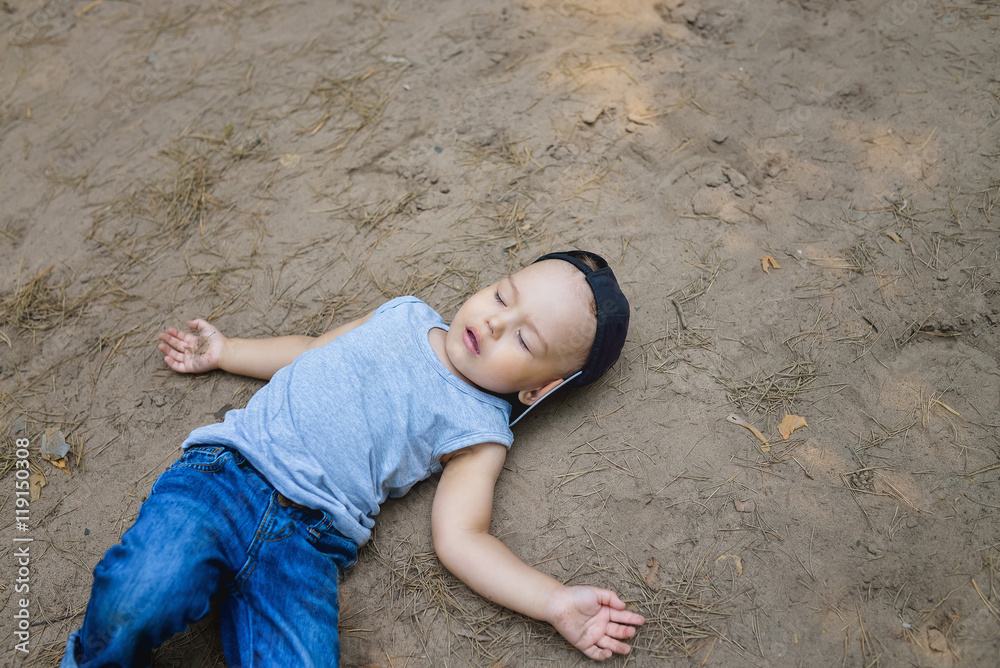 Little boy laying on ground pretending sleep or unconscious - obrazy, fototapety, plakaty 