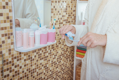 Closeup photo of man putting toothpaste on toothbrush at bathroom photo