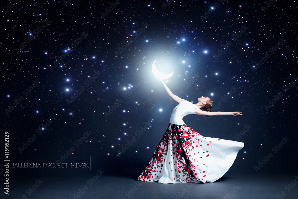 Naklejka premium Young ballerina in a beautiful dress is dancing in a dark photostudio
