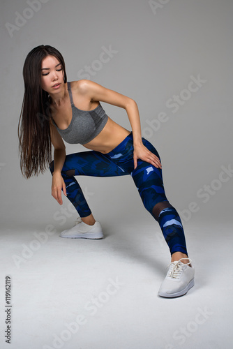 Beautiful Fit Woman in Camo Training Pants and White Sneakers Stretching Isolated On Gray Background