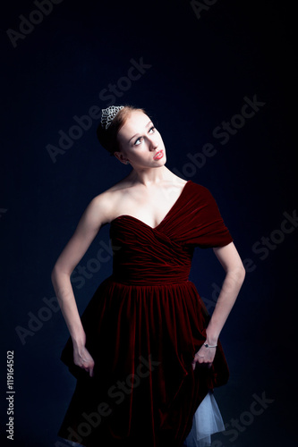 Young ballerina in a beautiful dress is dancing in a dark photostudio
