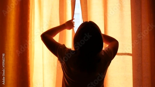 the girl opens the curtains on a Sunny day