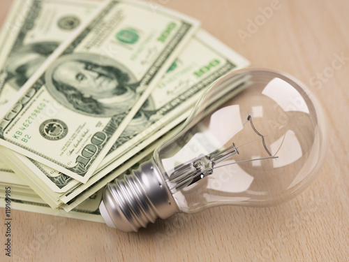 Light bulb in front of dollar bill stack