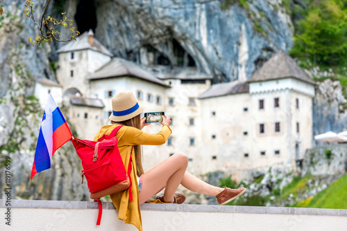 Young female traveler photographing with phone Predjama castle. This castle is a famous tourist attraction and a travel destination in Slovenia photo