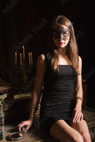 Fashion sexy brunet woman wearing black dress and mask at bedroo photo