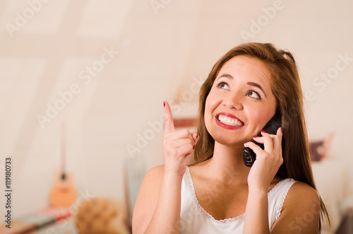 Young attractive woman wearing white top talking on phone while smiling  facing camera