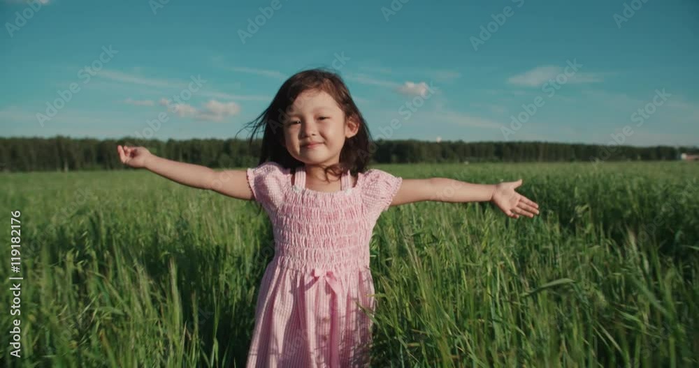 little Asian girl running in a green field of young wheat,slow motion