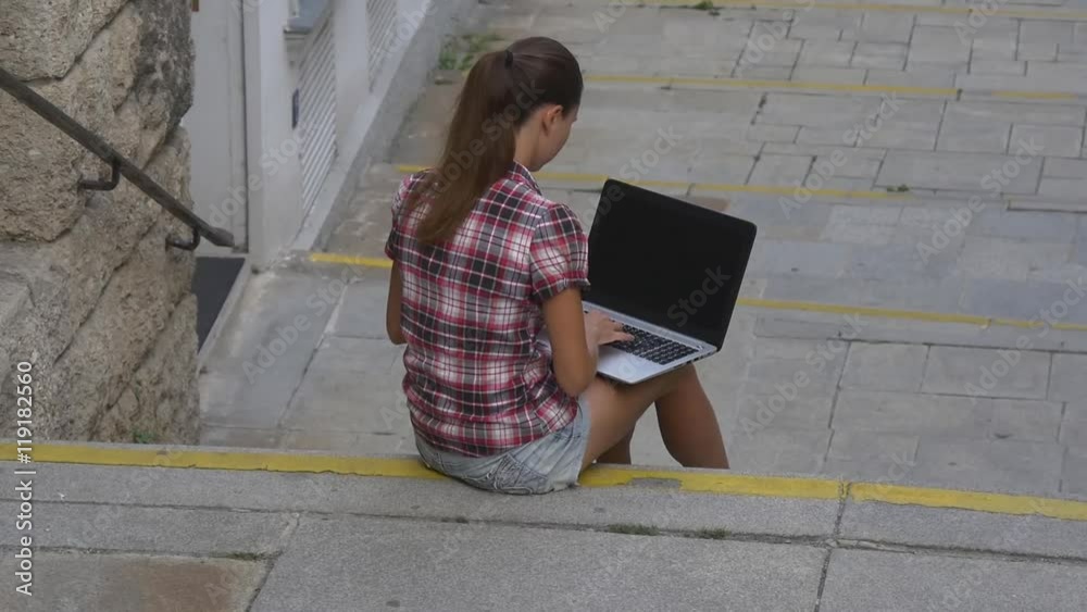 Woman typing on laptop keyboard sitting on the stairs Woman typing on laptop keyboard sitting on the stairs