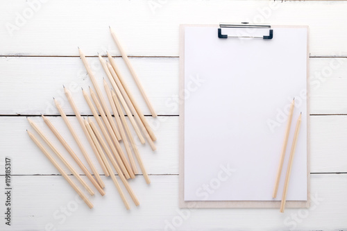 White clipboard with blank paper and pencils on white wood