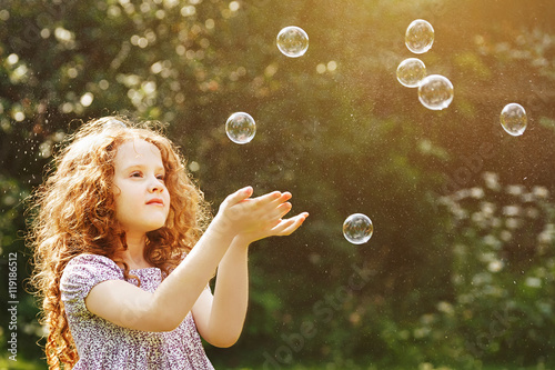 Curly little girl catch a soap bubbles.