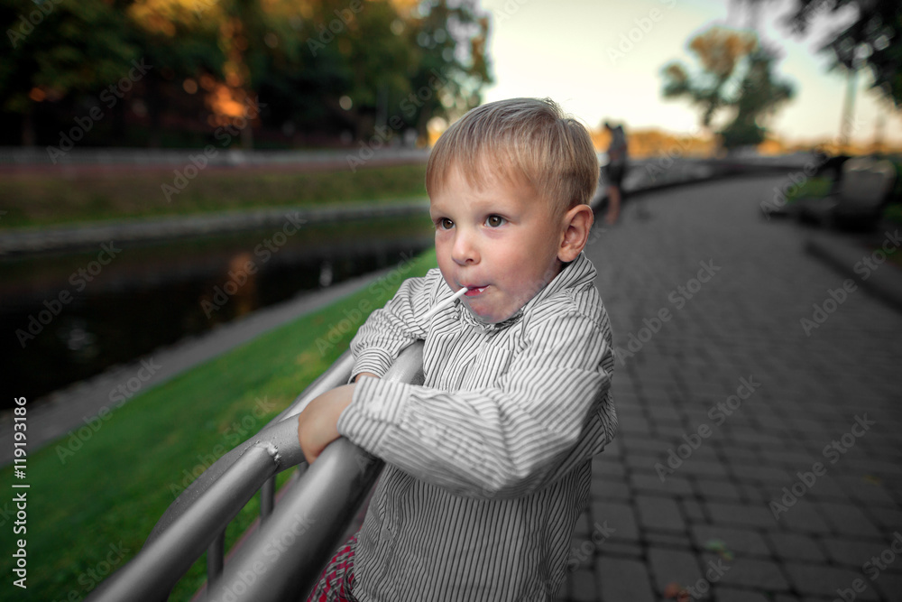 boy with a sucking candy walks in the park in the summer boy with a sucking candy walks in the park in the summer