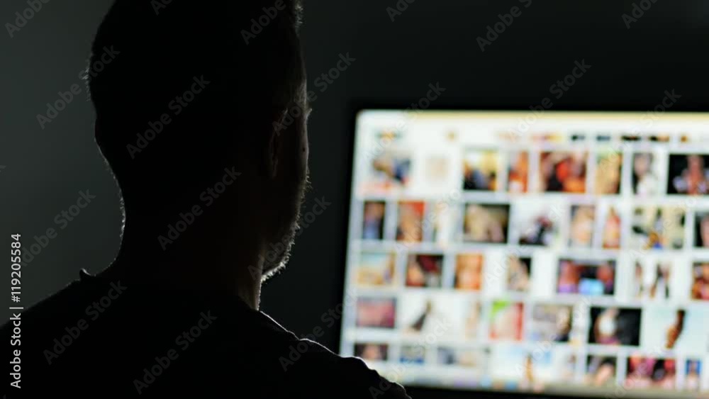 man surfing watching pornography site on the web looking for virtual sex at  night in a dark room,screen is out of focus ,useful to represent internet  easy porn accessibility and social isuue