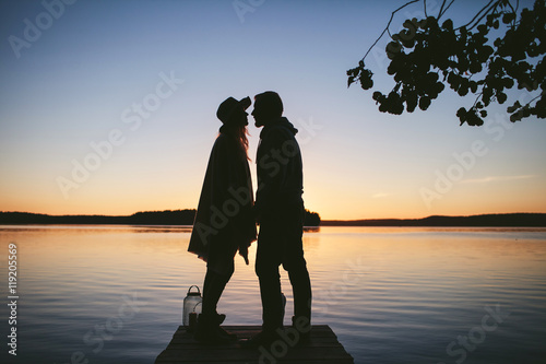woman and man are holding hands on a pier at the lake with sunset views