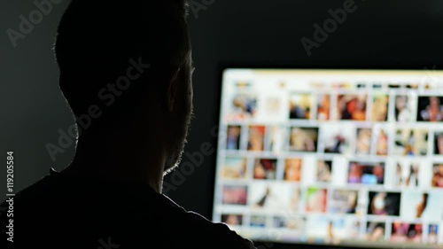 man surfing watching pornography site on the web looking for virtual sex at night in a dark room,screen is out of focus ,useful to represent internet easy porn accessibility and social isuue