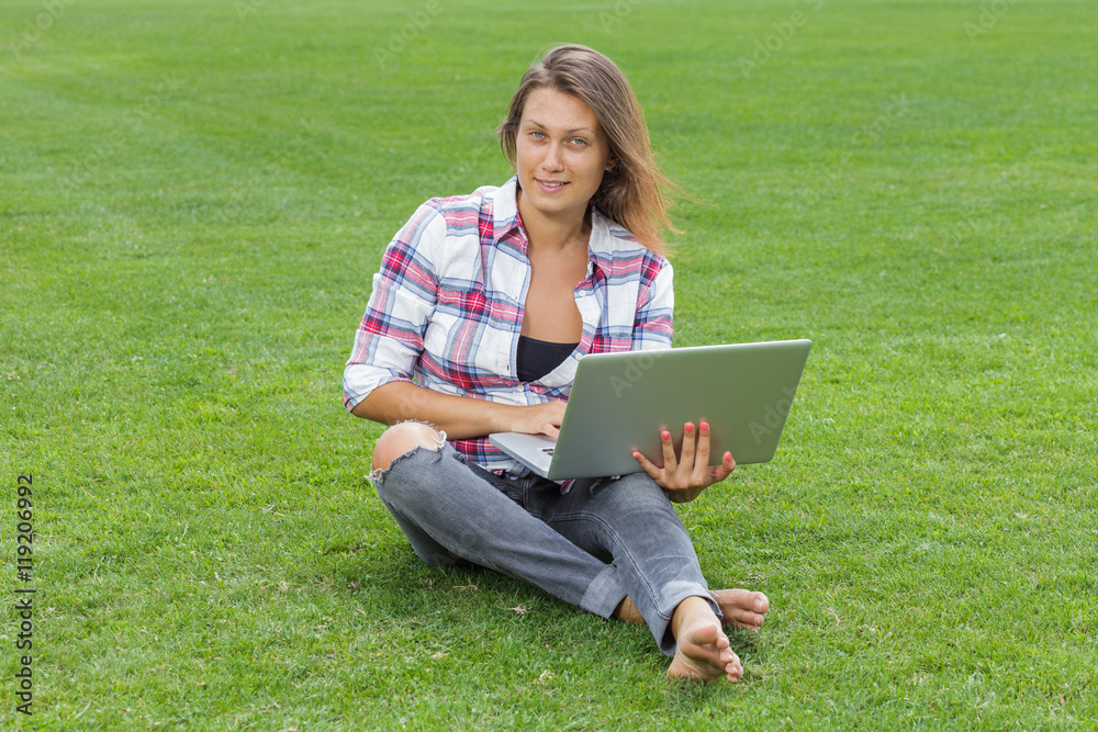 Young woman with laptop sitting on green grass and working outside Young woman with laptop sitting on green grass and working outside