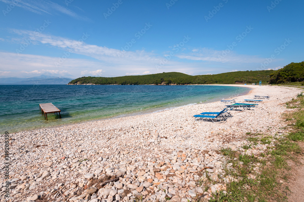 Obraz premium Sun beds on pebbly beach with crystal clear water. Corfu, Greece.