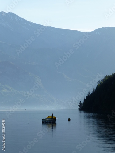 Lone fisherman in boat on the calm waters of Brienzersee, Switzerland on a hazy morning in late Spring
