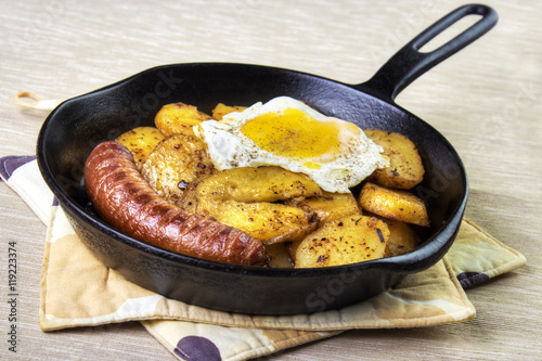 Serving pan fried potatoes , sausage and egg on cast iron skillet