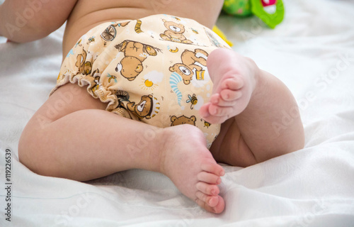 Tableau sur toile baby in modern eco stacks of cloth diapers and replacement bushings selective focus close-up on bright background, little cute foot kid, the concept of health