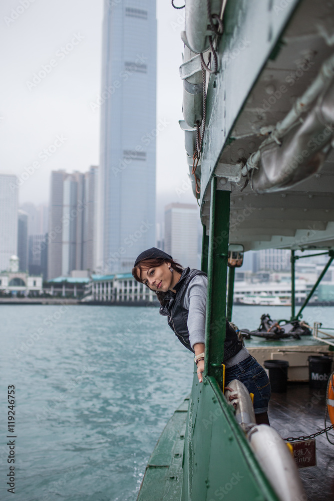 Girl tourist on background of a big city with skyscrapers, looking at the Hong Kong city from the boat