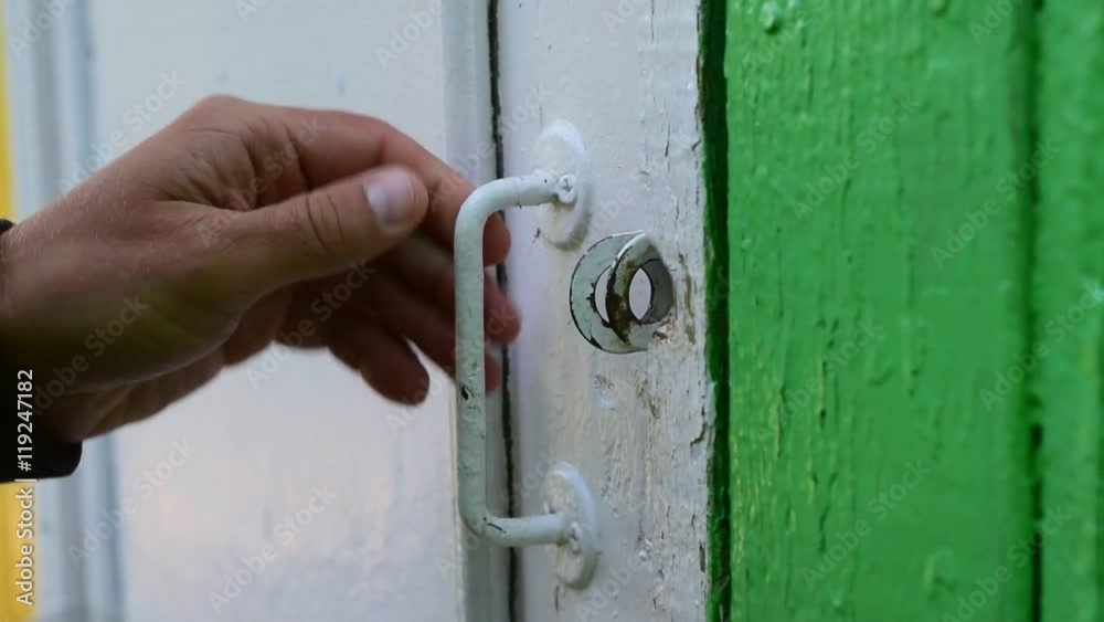 Closeup of male hands quickly open a metal padlock with a key on an old wooden door and a person goes through doorway Closeup of male hands quickly open a metal padlock with a key on an old wooden door and a person goes through doorway