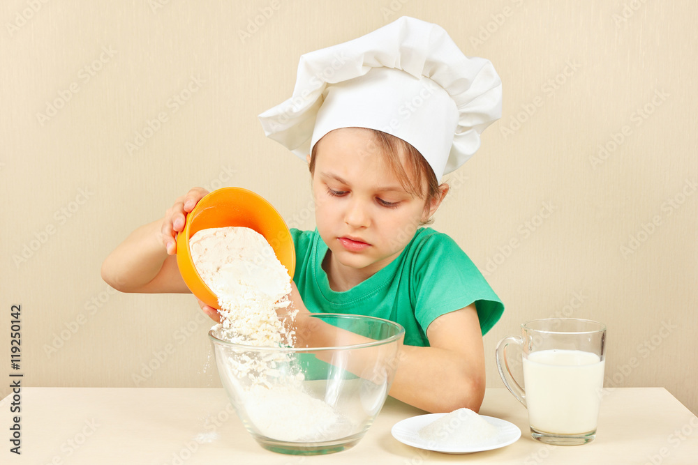 Young boy in chefs hat pours flour for baking the cake Young boy in chefs hat pours flour for baking the cake