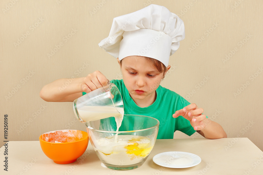 Little boy in chef hat pours milk for baking the cake Little boy in chef hat pours milk for baking the cake