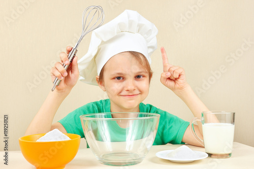 Young smiling chef at the table with ingredients is going to cook a cake