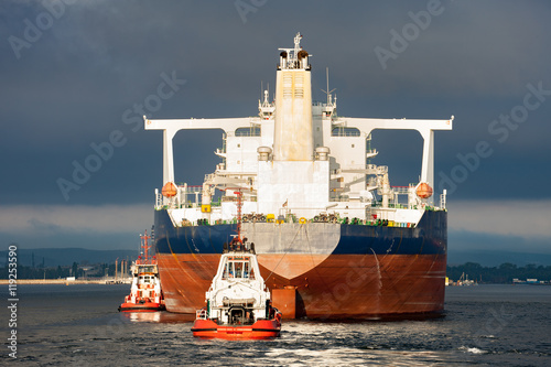 Tugboats towing a large tanker ship in port.
