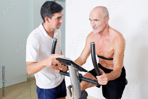 Elderly senior with coach on indoor bike