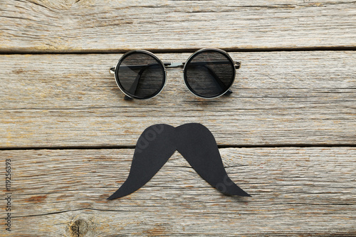 Black sunglasses and mustache on a grey wooden table