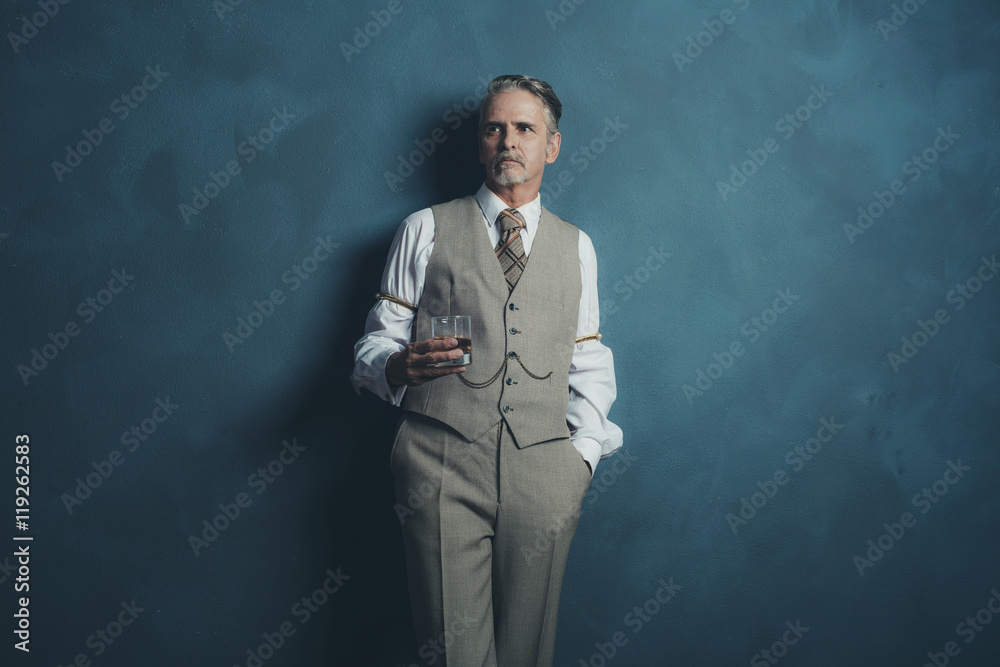 Vintage 1920s businessman with glass of whiskey leaning against