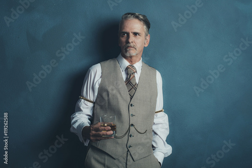 Vintage 1920s businessman with glass of whiskey leaning against