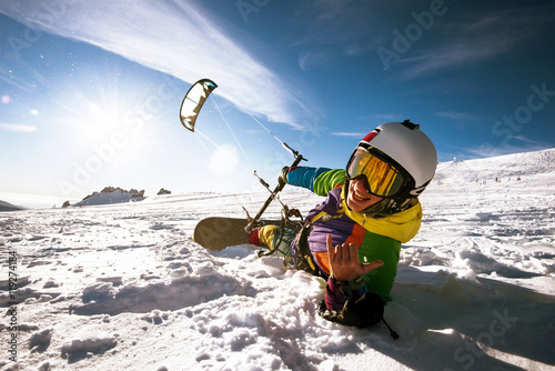 Happy snowboarder lies and holds snowkite