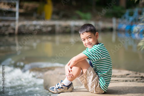 Little boy sitting on the rock looking at waterfall alone color spot photo