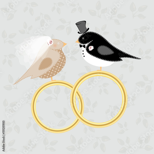 Birds in costumes of the bride and groom sit at the wedding rings